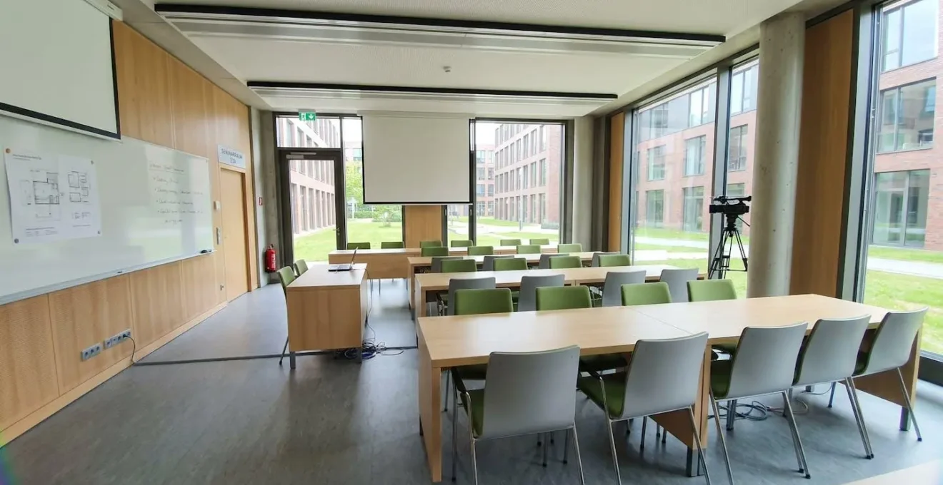 Moderner heller Seminarraum einer Universität, leer, zeitgenössisches Mobiliar, grosse Fenster mit Tageslicht, minimalistisches Design, Videokamera auf Stativ in der Ecke